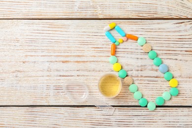 Bottle made of pills, measuring cup with syrup on white wooden table, flat lay and space for text. Cold medicine