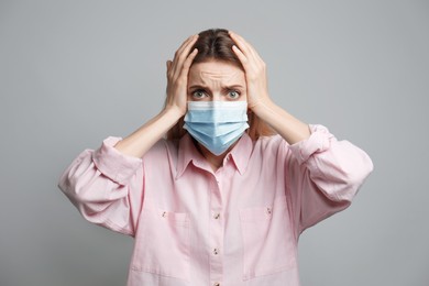 Young woman in protective mask feeling fear on grey background