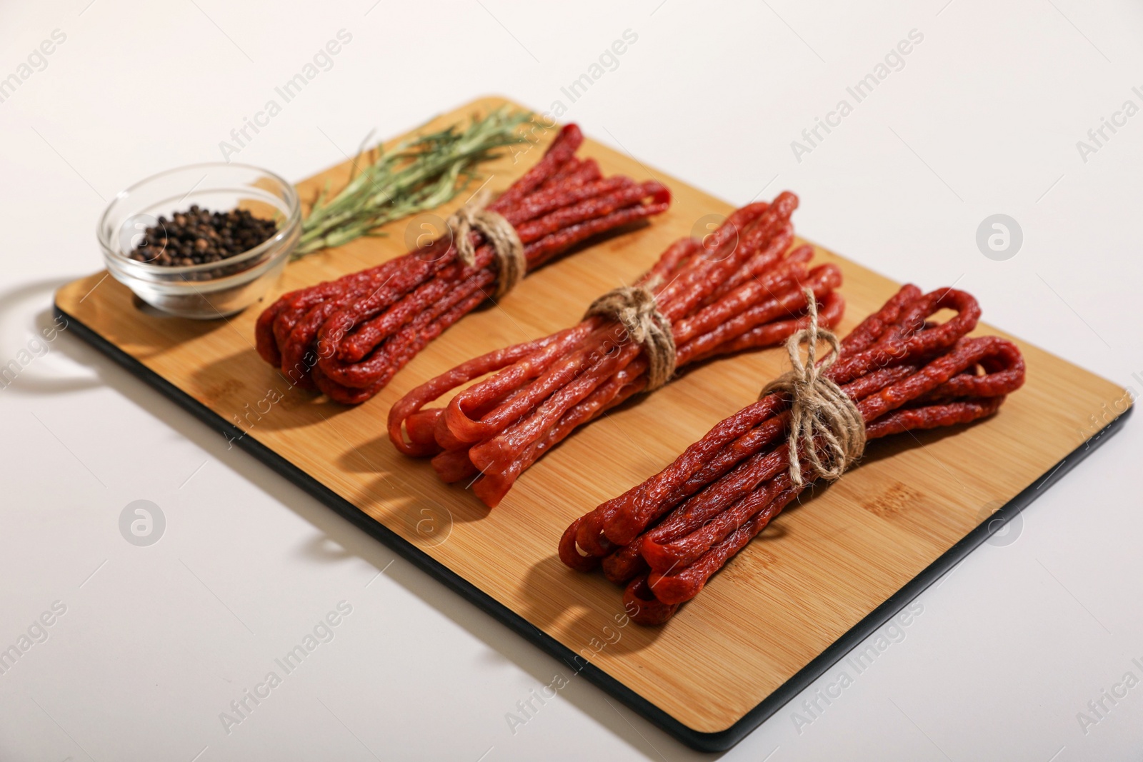 Photo of Bundles of delicious kabanosy with peppercorn and rosemary on white background