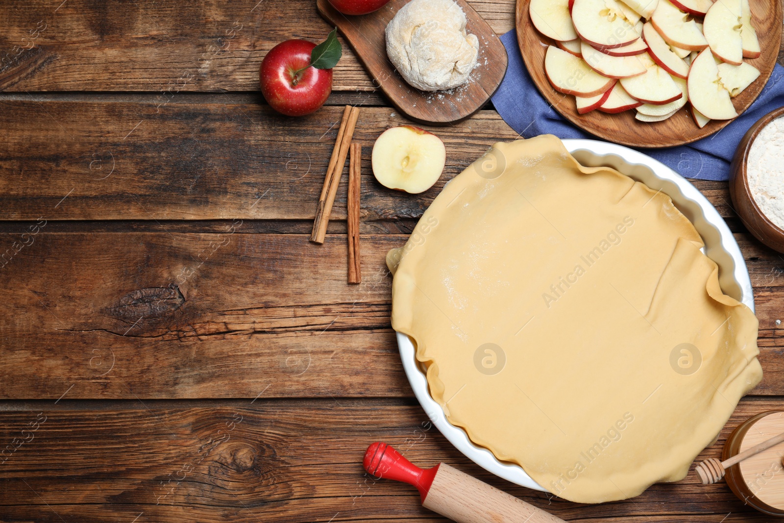 Photo of Flat lay composition with raw dough and ingredients on wooden table, space for text. Baking apple pie