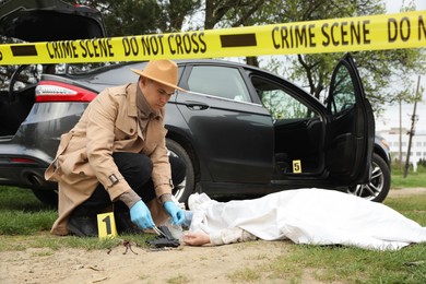 Photo of Investigator in protective gloves working at crime scene with dead body outdoors