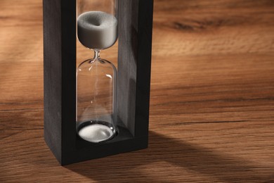 Photo of Hourglass with white flowing sand on wooden table, closeup. Space for text