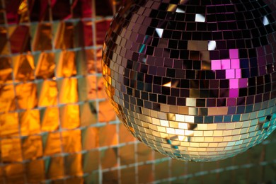 Photo of Shiny disco ball against foil party curtain under orange light. Space for text