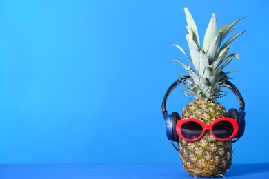 Photo of Pineapple with headphones and sunglasses on color background. Space for text