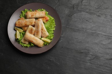Photo of Plate with tasty fried spring rolls, lettuce and lime, on dark textured table, top view. Space for text