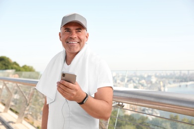 Photo of Handsome mature man in sportswear with mobile phone on bridge, space for text. Healthy lifestyle