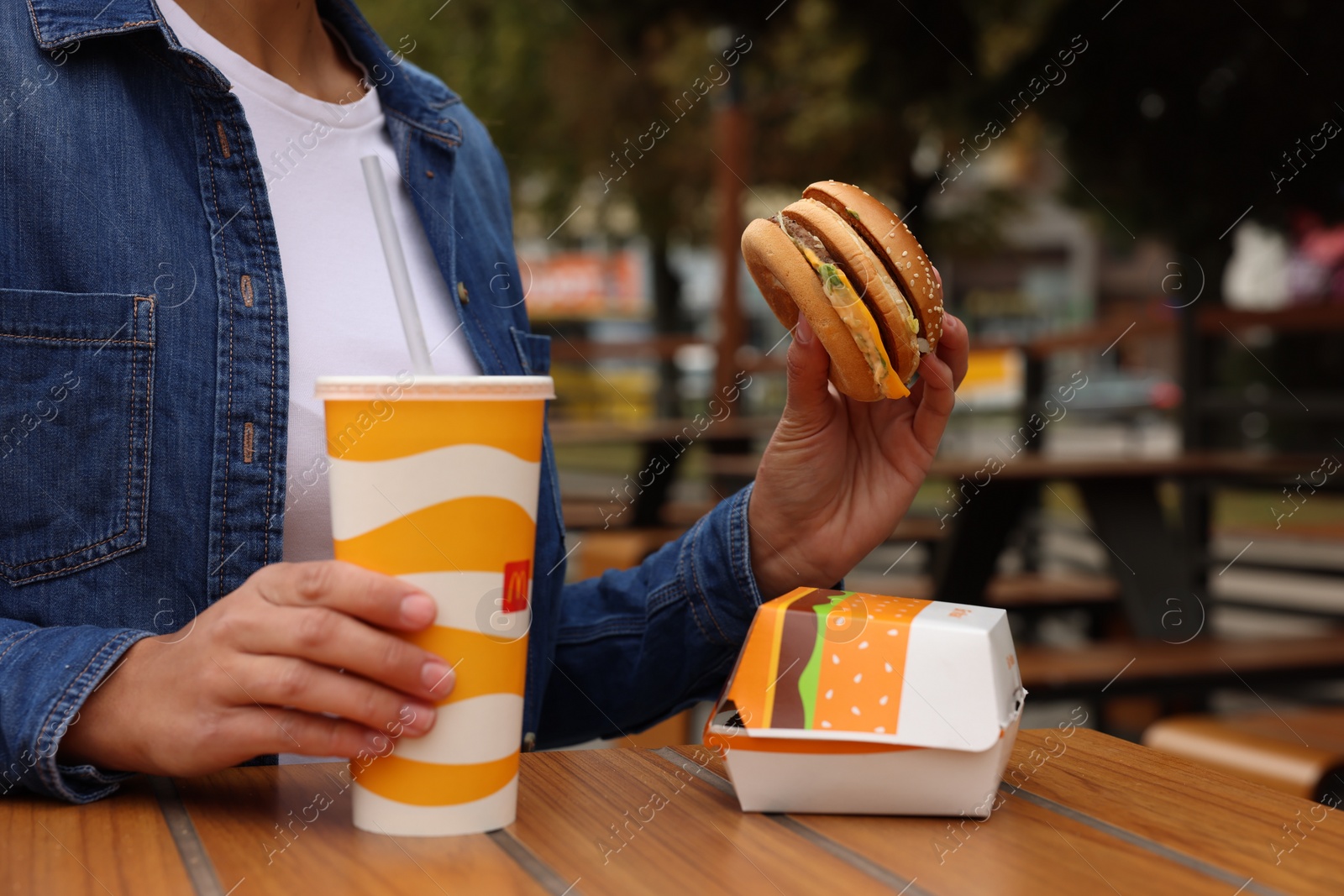 Photo of Lviv, Ukraine - October 9, 2023: Woman with McDonald's burger and drink at wooden table outdoors, closeup