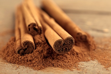 Photo of Aromatic cinnamon sticks and powder on wooden table, closeup