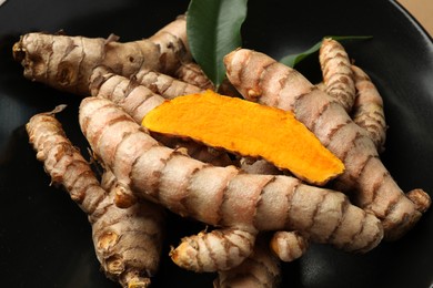 Many raw turmeric roots in black bowl, closeup