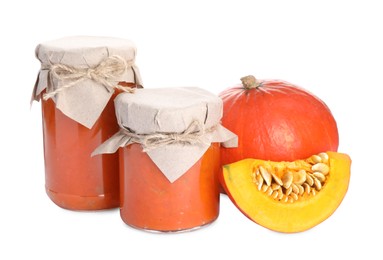 Photo of Jars of pumpkin jam and fresh pumpkin on white background