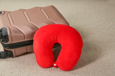 Photo of Red travel pillow and suitcase on beige rug