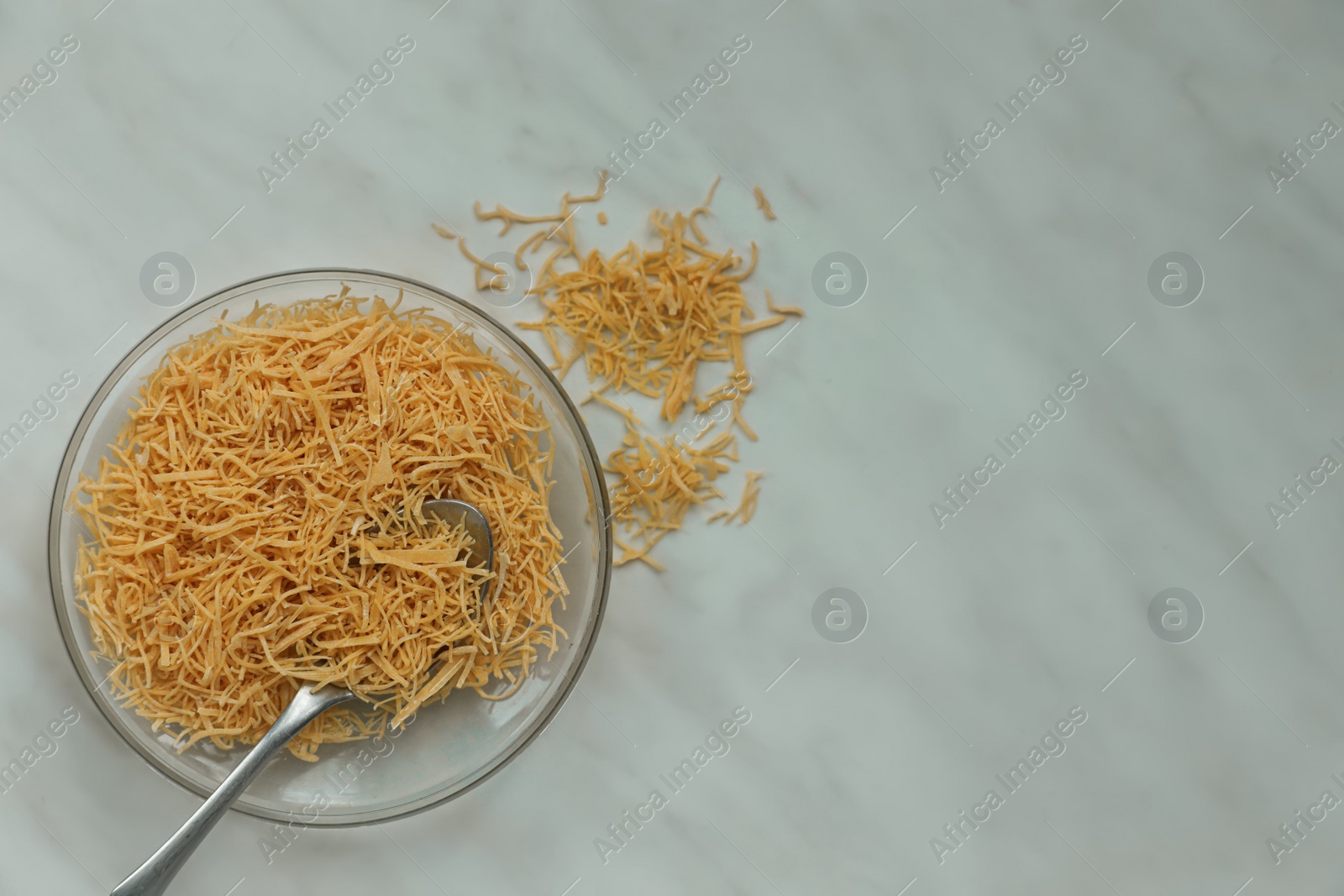 Photo of Bowl of uncooked vermicelli and spoon on white marble table, flat lay. Space for text