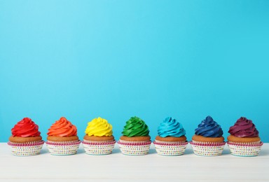 Many delicious colorful cupcakes on white table against light blue background. Space for text