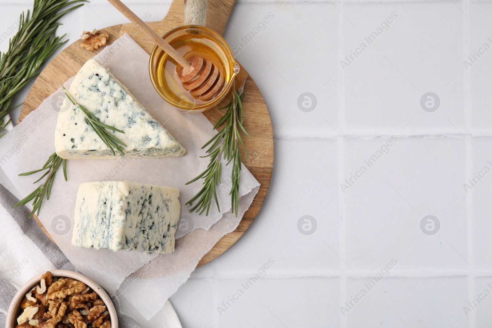 Photo of Tasty blue cheese with rosemary, honey and walnuts on white tiled table, flat lay. Space for text