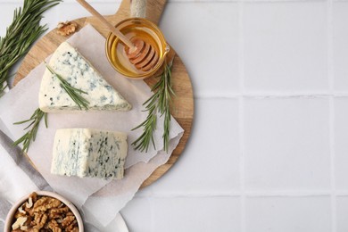 Tasty blue cheese with rosemary, honey and walnuts on white tiled table, flat lay. Space for text