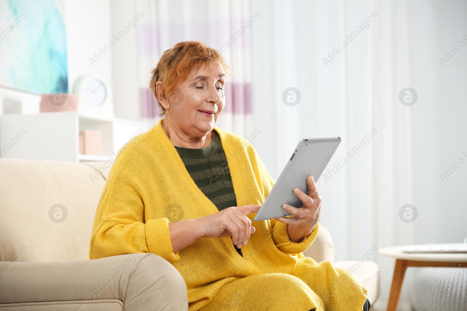 Photo of Elderly woman using tablet PC on sofa in living room