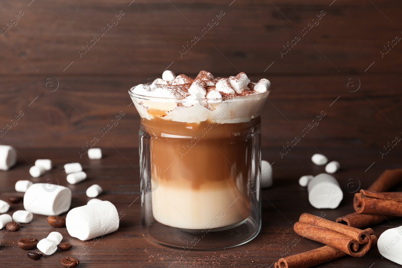 Photo of Glass with delicious coffee drink, marshmallows and cinnamon sticks on wooden table