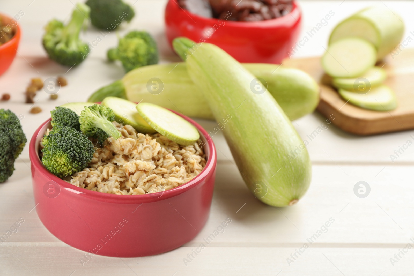 Photo of Feeding bowl with oatmeal porridge and vegetables on white wooden table, closeup. Natural pet food