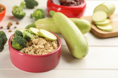 Feeding bowl with oatmeal porridge and vegetables on white wooden table, closeup. Natural pet food