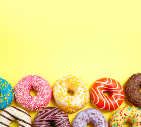 Delicious glazed donuts on yellow background, flat lay. Space for text