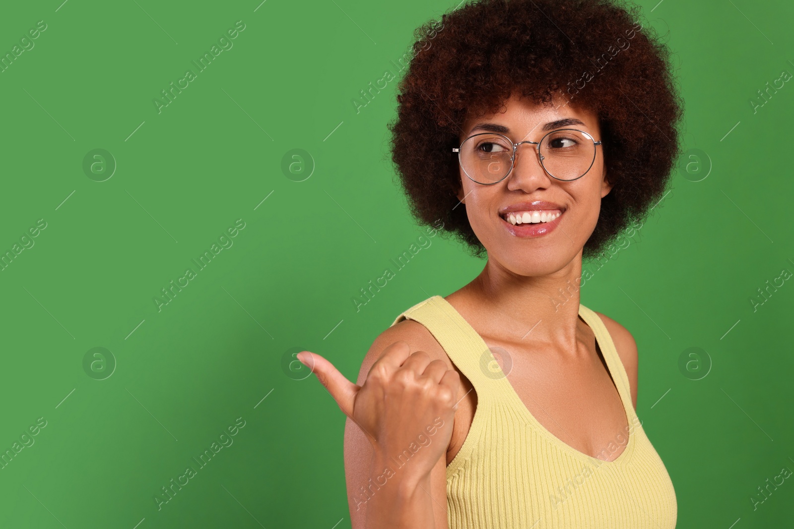 Photo of Happy young woman in eyeglasses pointing at something on green background. Space for text