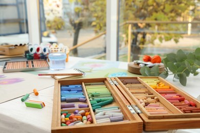 Photo of Artist's workplace with drawings, soft pastels and color pencils on table indoors