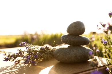 Photo of Stack of spa stones on wooden table in lavender field. Harmony and zen