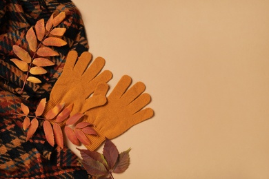 Photo of Stylish woolen gloves, scarf and dry leaves on beige background, flat lay. Space for text