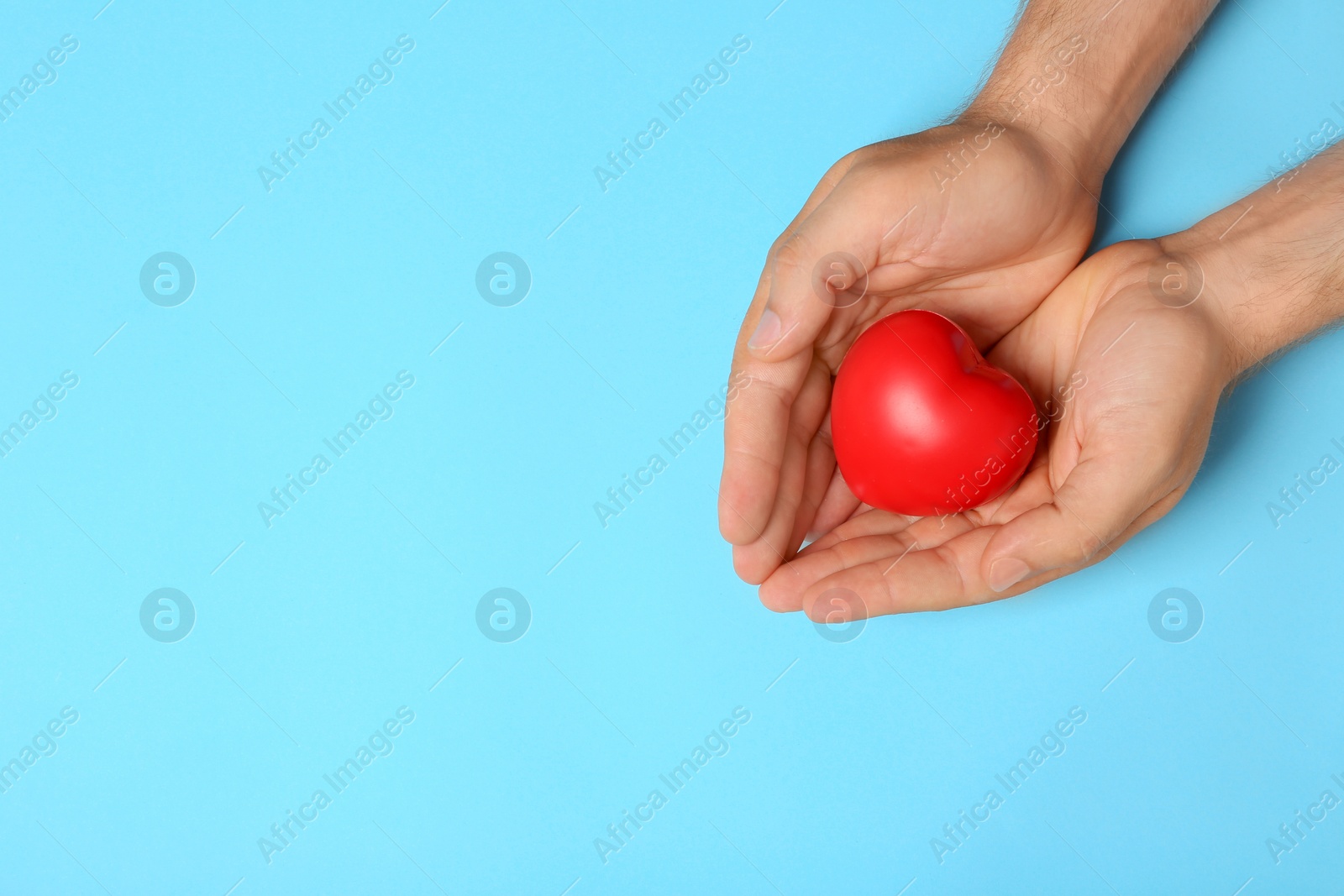 Photo of Young man holding red heart on light blue background, top view with space for text. Donation concept