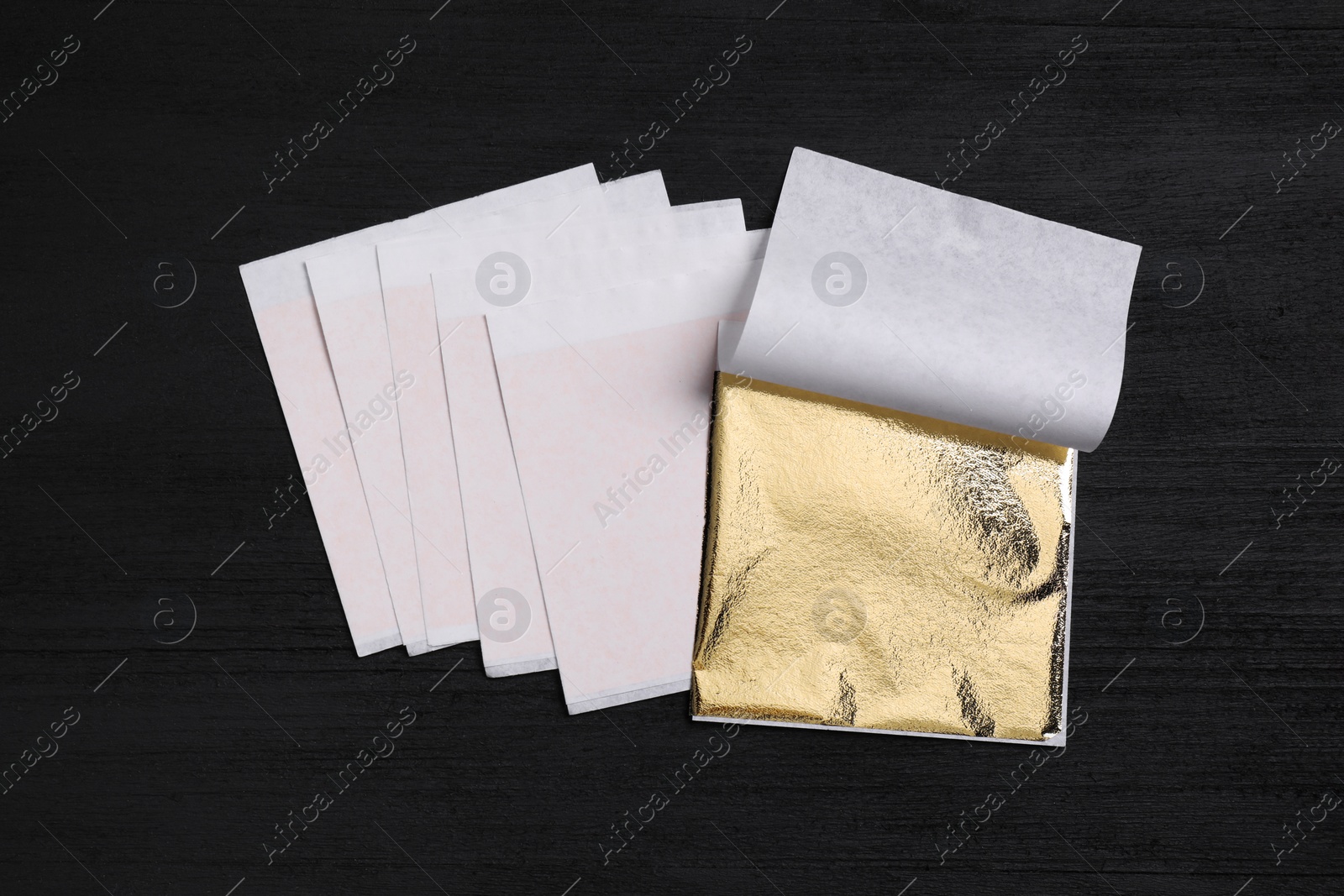 Edible gold leaf sheets on black wooden table, flat lay Photo of Edible gold leaf sheets on black wooden table, flat lay