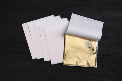 Photo of Edible gold leaf sheets on black wooden table, flat lay