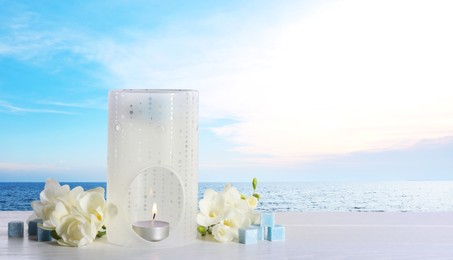 Image of Composition with aroma lamp on white wooden table near sea , space for text. Banner design