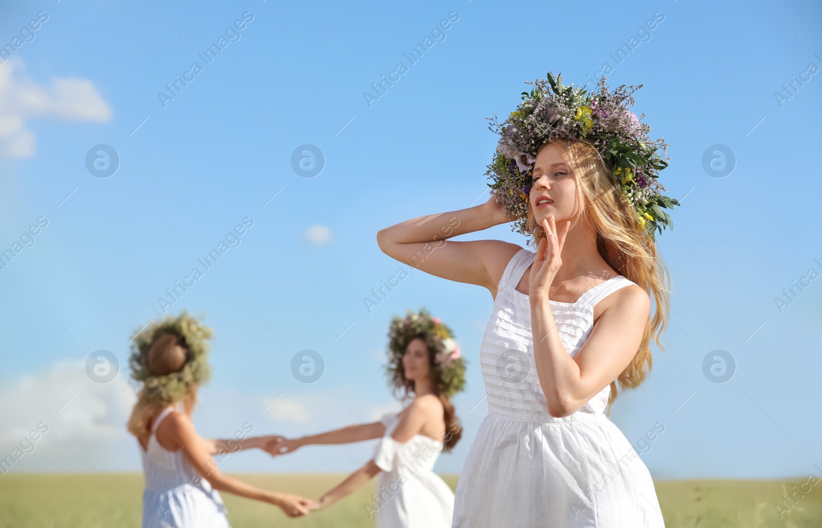 Photo of Young women wearing wreaths made of beautiful flowers in field on sunny day