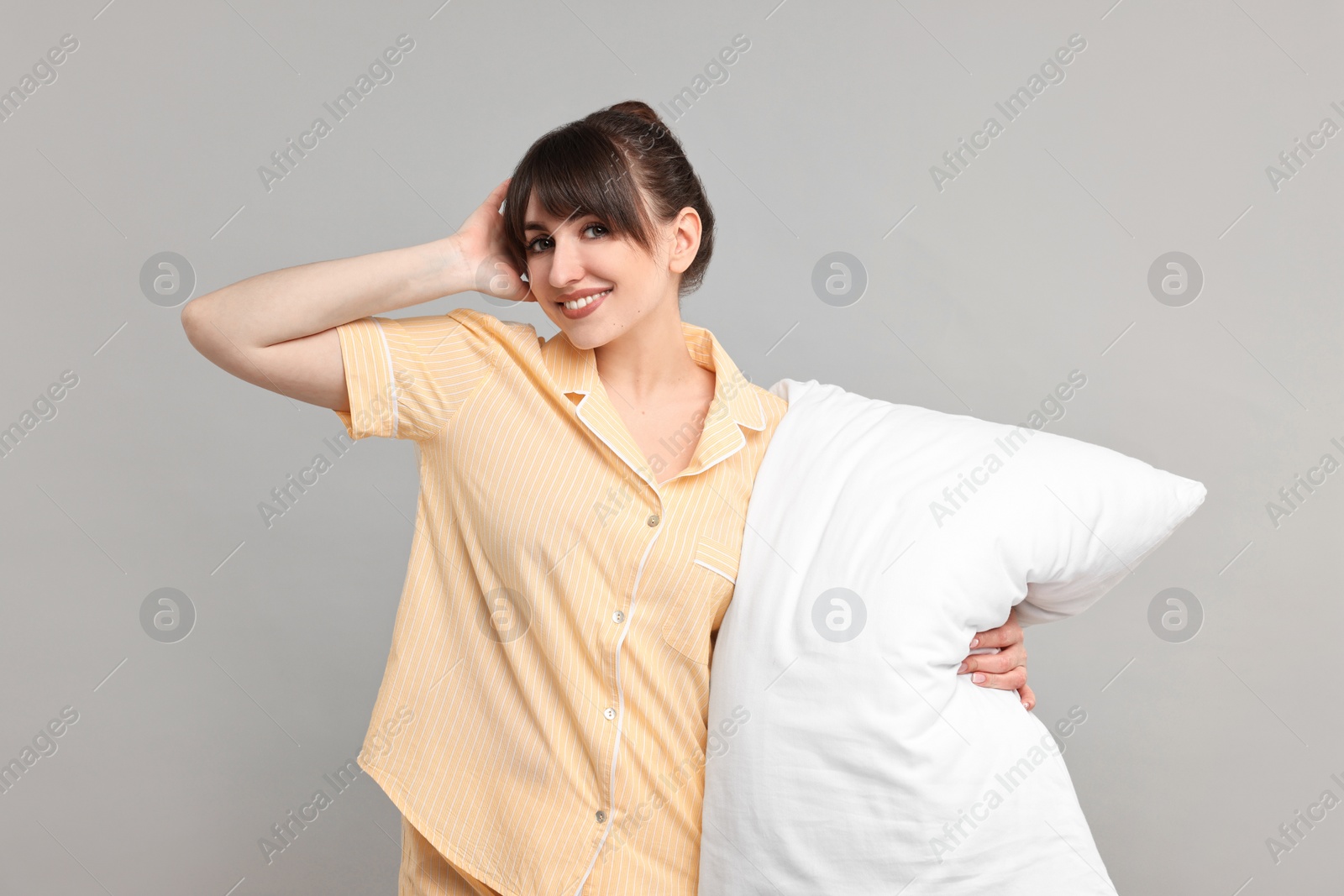 Photo of Happy woman in pyjama holding pillow on grey background