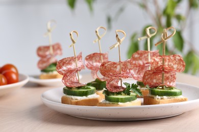 Photo of Tasty canapes with salami, cucumber and cream cheese on light table, closeup