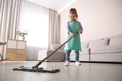Photo of Little girl mopping floor in living room at home