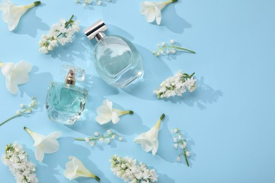 Luxury perfumes and floral decor on light blue background, flat lay. Space for text