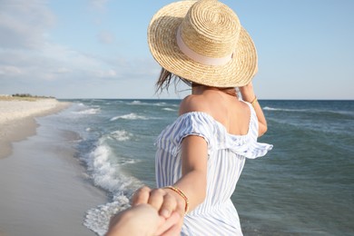 Photo of Woman with straw hat holding her lover's hand near sea on sunny day