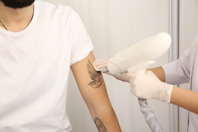 Young man undergoing laser tattoo removal procedure in salon, closeup