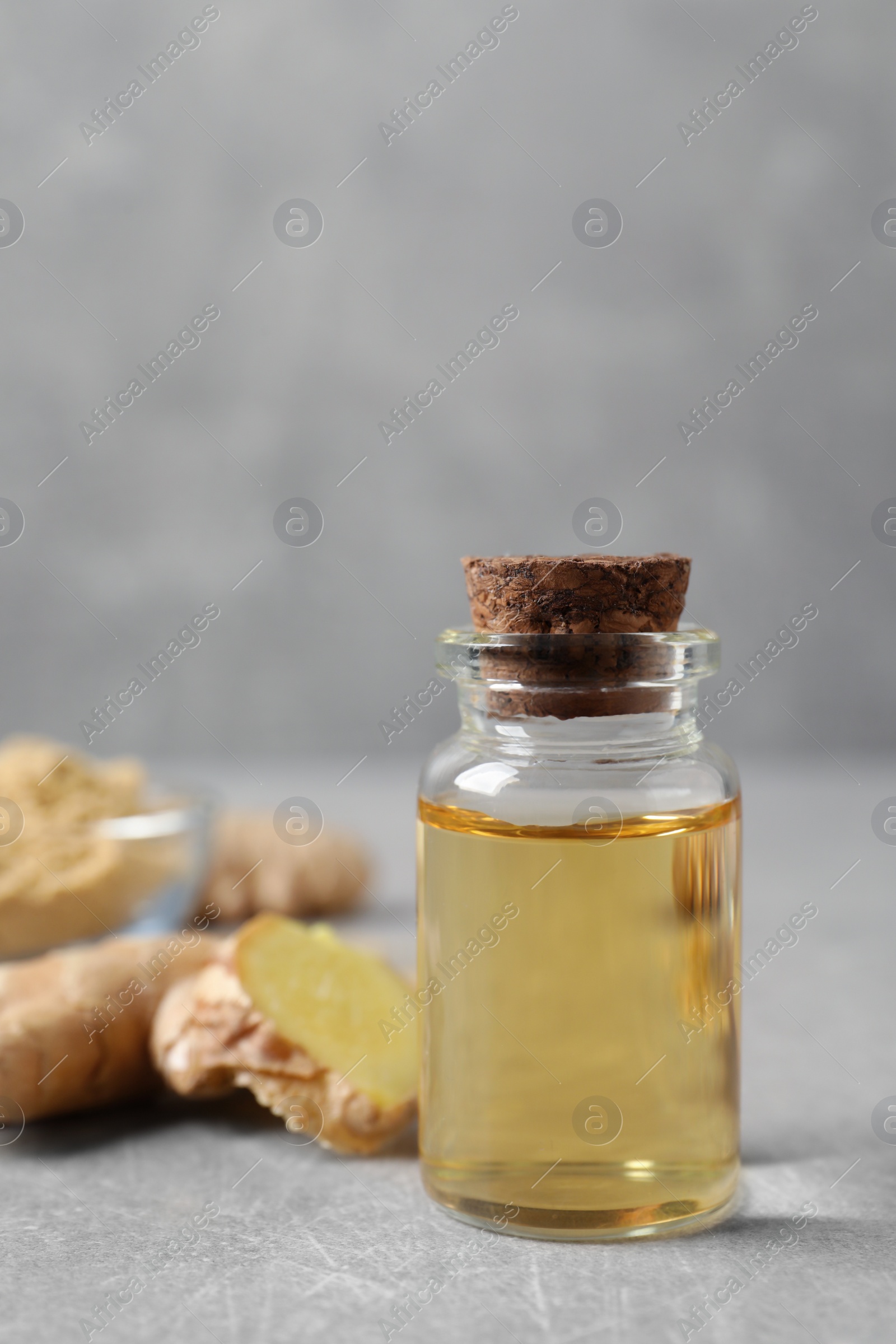 Photo of Glass bottle of essential oil and ginger root on grey table