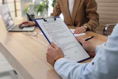 Man reading employment agreement at table in office, closeup. Signing contract