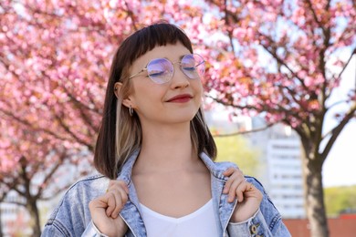 Photo of Beautiful young woman near blossoming sakura trees in park
