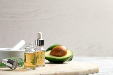 Photo of Bottle of essential oil, pipette and fresh avocado on table, closeup. Space for text