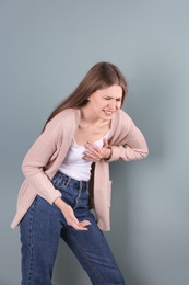 Young woman having heart attack on color background