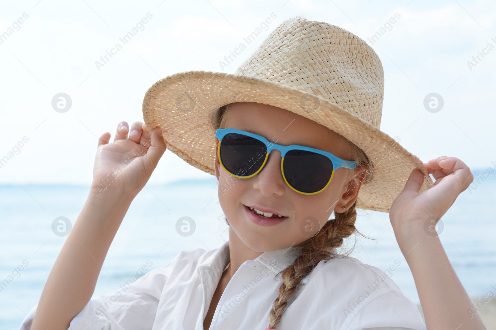 Photo of Little girl wearing sunglasses and hat at beach on sunny day