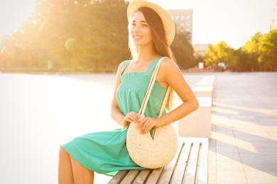 Photo of Young woman with stylish straw bag on bench outdoors