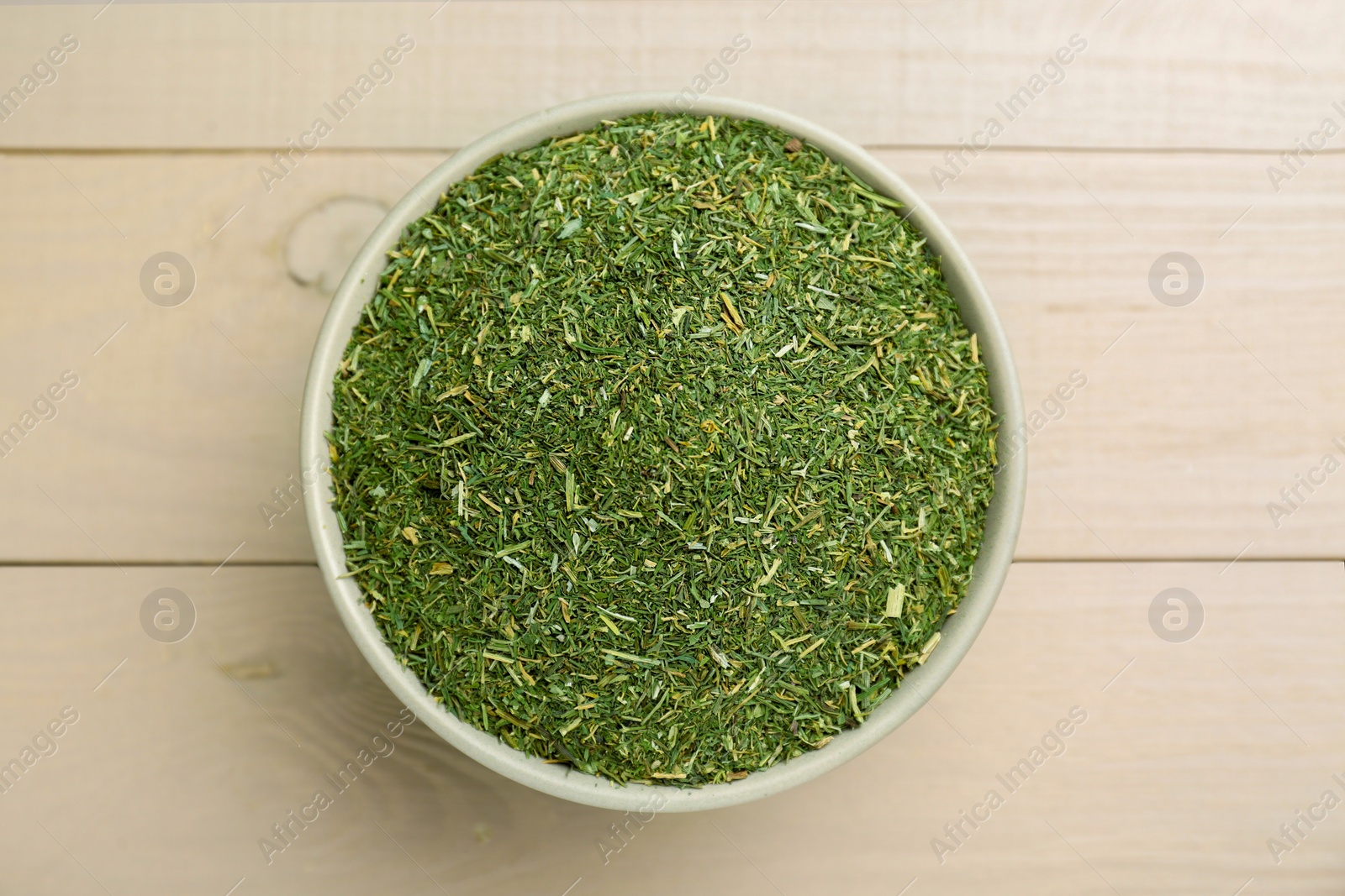 Photo of Dried dill in bowl on white wooden table, top view