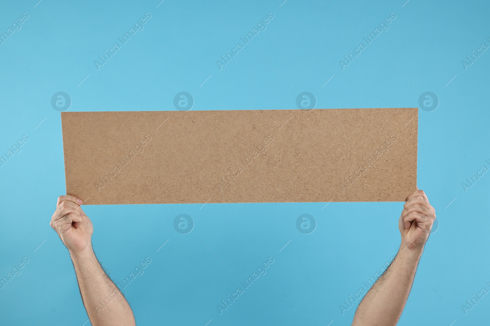 Photo of Man holding blank cardboard banner on light blue background, closeup. Space for text