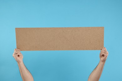 Man holding blank cardboard banner on light blue background, closeup. Space for text