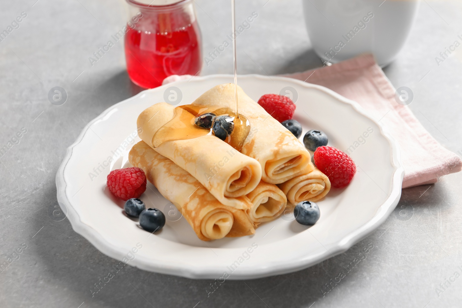 Photo of Pouring honey on thin pancakes with berries, closeup